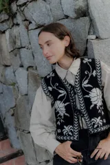 Chaleco tejido de punto con diseño floral en contraste, cierre frontal con lazos y terminaciones con guardas geométricas.