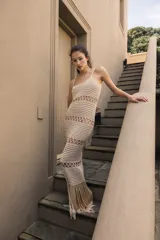 Vestido largo tejido a crochet color crudo, con breteles finos y diseño calado. Presenta flecos en el ruedo.