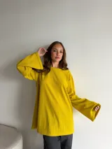 Buzo de punto morley color amarillo mostaza, con cuello redondo y mangas largas amplias de corte acampanado.