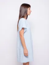 Vestido corto de corte holgado, color celeste, con cuello redondo fruncido y mangas cortas. Está confeccionado en una tela con textura diferenciada que le aporta relieve.