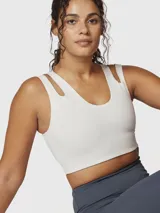 Top deportivo de sujeción media, color blanco, confeccionado en tejido suave y elástico con Aloe Vera. Presenta un diseño de espalda cruzada y dos tiras con aberturas en los hombros.