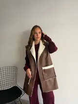 Chaleco largo de eco cuero color marrón con interior y detalles de corderito en solapas y bolsillos frontales.