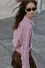 Camisa de manga larga con estampado de cuadros en tonos rosados y negros. Presenta cuello solapa, bolsillo delantero de plastrón, cierre frontal con botones y detalle de laterales ajustables con lazos.