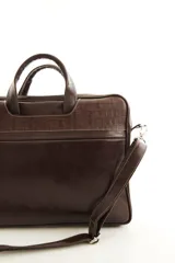 Portafolio de cuero vacuno marrón, con doble asa superior, correa ajustable desmontable y bolsillo frontal con cierre. Presenta detalles de textura símil reptil en la parte superior.