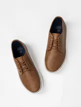 Zapatilla de estilo casual con cordones, confeccionada en cuero sintético color marrón con suela de goma blanca.