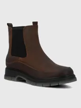 Bota tipo Chelsea de cuero marrón con paneles laterales elásticos en color negro. Presenta costuras reforzadas en el contorno y una suela robusta de poliuretano con base dentada en tono gris translúcido.