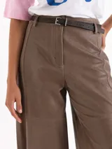 Pantalon de cuero ovino marron, de tiro alto, silueta wide-leg con recortes horizontales a la altura de la rodilla y bolsillos aplicados en la espalda. Incluye un cinturon de cuero al tono.