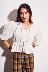 Blusa negra de algodón con diseño de broderie, mangas tres cuartos abullonadas, cierre frontal con botones y detalle de cordón ajustable en la cintura.