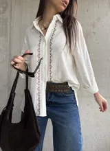 Camisa blanca de tejido liviano y calce relajado, con manga larga y detalle de puntilla y bordado en contraste a lo largo de la botonadura frontal.