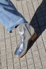 Botas plateadas de cuero con caña media, punta cuadrada, cierre lateral y diseño bordado estilo western.