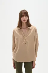 Blusa holgada de poliéster color beige, con cuello camisero, escote en V con botones frontales y mangas largas.