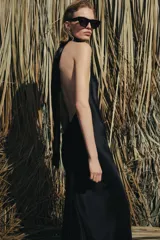 Vestido largo de satén negro con cuello halter subido y espalda descubierta. Presenta un diseño fluido con bajo en línea evasé.