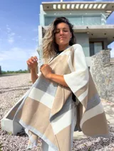 Ruana tejida con diseño de franjas horizontales en tonos beige, gris y crudo, de corte abierto y caída fluida.
