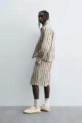 Bermuda de hombre color beige con estampado de rayas verticales azules con efecto desgastado. Corte relaxed fit, con cierre frontal de cremallera y botón, bolsillos delanteros y bolsillos traseros de plastrón.