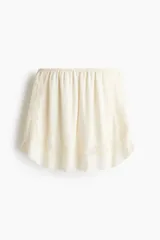 Minifalda holgada de viscosa color marfil con inserciones de encaje. Presenta cintura elástica con ribete de picot y frunces en todo el contorno, silueta ligeramente acampanada y dobladillo redondeado con abertura en cada lateral.