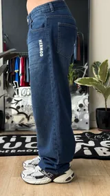 Pantalón de jean azul oscuro de corte wide leg, con diseño holgado y tiro medio. Presenta un pequeño bordado con alas en el bolsillo delantero.