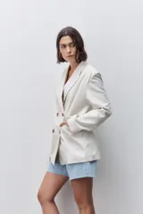 Blazer de silueta amplia y largo por debajo de la cadera, color marfil, confeccionado en tela suave y liviana. Presenta cuello con solapas, hombreras, manga larga y cierre cruzado con botones carey.