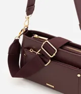 Cartera bandolera de poliuretano color marrón oscuro, con estructura firme y tamaño mediano. Cuenta con un bolsillo frontal con cierre, herrajes metálicos dorados, cierre principal y correa ajustable y desmontable.