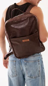 Mochila de cuero genuino color marrón, con diseño minimalista, compartimento principal con cierre, bolsillo frontal con etiqueta de marca y correas ajustables.