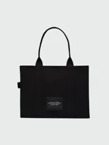 Bolso tipo tote de Marc Jacobs, confeccionado en lona resistente de color negro. Presenta el nombre del modelo y la marca estampados en blanco en la parte frontal, con doble asa superior.