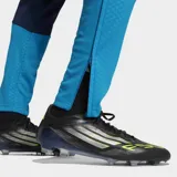 Pantalón de entrenamiento Adidas Tiro España 26, color azul marino con detalles en celeste y franjas laterales en amarillo y rojo. Incluye logo de Adidas en amarillo y tecnología Formotion.