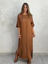 Vestido marrón de corte recto y largo midi, con mangas 3/4 y cuello redondo. Presenta aberturas laterales en el ruedo.