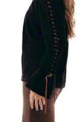 Camisa manga larga de gamuza ovina negra, con cuello clásico y cierre frontal de broches a presión. Presenta detalles de aberturas (cutouts) en las mangas entrelazadas con pasamanería de cuero en tono chocolate.