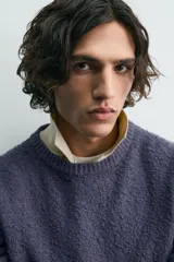 Jersey de hombre de corte relajado, color azul oscuro o morado apagado, con textura rizada (bouclé) y cuello redondo.