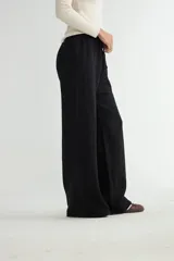 Pantalón de punto color crema, de corte recto y holgado, con cintura elástica y cordón ajustable. Presenta costuras verticales decorativas a lo largo de las piernas.