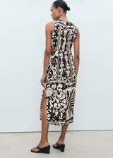 Vestido midi sin mangas con cuello redondo y aberturas laterales tipo cut-out en la cintura. Presenta un diseño recto con estampado botánico en contraste y cierre de cremallera en la parte posterior.