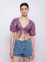 Top estampado con flores rosas, hojas verdes y líneas negras, de manga corta abullonada con nudo en el escote.