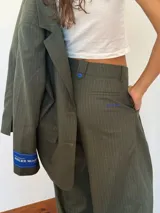 Blazer de sastrería con diseño oversize y hombreras pronunciadas. Presenta un estampado de rayas verticales finas, cierre frontal con botones nacarados y forrería a contratono. Incluye una etiqueta bordada decorativa en la manga.