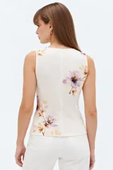Chaleco de viscosa color crudo con estampado floral en tonos morados y marrones, escote en V, sin mangas y cierre frontal con botones.