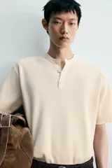 Camiseta regular fit de punto tejido en hilatura de algodón de color beige, con cuello redondo y cierre frontal de botonadura tipo panadero, manga corta y acabados en rib.