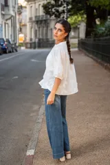 Blusa de algodón color blanco con bordado sutil en relieve, cuello redondo, cierre frontal con botones y mangas tres cuartos con terminación elástica.