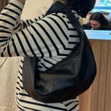 Cartera negra de cuero con forma de media luna y asa corta.