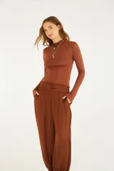 Pantalón de tiro alto y silueta amplia, estilo aladín, color marrón. Cuenta con cintura de pala ancha fruncida, bolsillos laterales y puños elásticos en los tobillos.