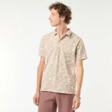 Remera polo de piqué color beige con estampado de palmeras y motivos playeros en blanco.