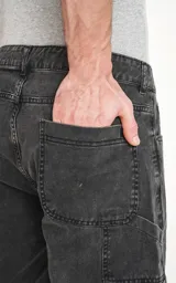 Bermuda de denim color negro lavado, estilo carpintero con bolsillo lateral utilitario y calce oversize.