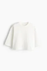 Remera oversized confeccionada en punto de algodón suave, de corte boxy con cuello redondo, hombros caídos y media manga.