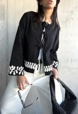 Chaqueta negra con escote redondo y cierre frontal con lazos. Presenta bordado de hojas blancas en los puños.