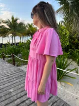 Vestido corto color beige de lino, con cuello mao, mangas cortas con volados, tablas en el canesú y falda escalonada con volantes.