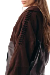 Campera bomber de cuero ovino negro combinada con gamuza chocolate, cuello solapa y cierre frontal de botones. Presenta mangas largas con detalles de costuras decorativas y bolsillos laterales ribeteados.