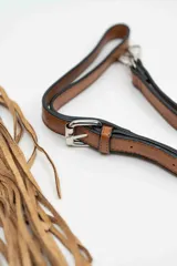 Cartera de gamuza color camel con diseño semicircular, decorada con flecos largos en el borde y tachas metálicas plateadas en la parte frontal. Incluye una correa larga ajustable y extraíble.