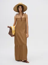 Vestido midi de denim color marrón, con corte holgado, breteles finos con lazos ajustables y detalle de volado en el ruedo.