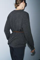 Jersey oversize de lana con escote en pico y manga larga. Incluye un cinturón fino de cuero en tono marrón con hebilla metálica dorada.