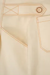 Bermuda de tiro alto en color crudo, confeccionada en lona de algodón. Presenta un corte acampanado con pliegues en la cintura, bolsillos delanteros inclinados y costuras decorativas en contraste color camel.