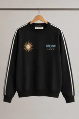 Buzo negro de cuello redondo con diseño deportivo, presenta una estampa de sol en el pecho izquierdo y el logo BHN DSG con estrellas en el derecho. Incluye franjas blancas laterales en las mangas y puños acanalados.