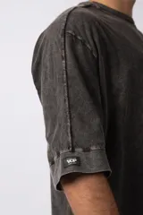 Remera de corte oversize con efecto de lavado gastado, confeccionada en algodón pesado. Presenta cuello redondo, mangas cortas con costuras visibles y un diseño amplio.