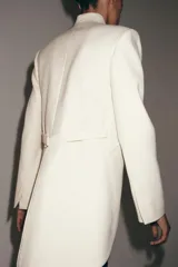 Blazer tipo frac de corte largo y diseño sin solapa. Presenta mangas largas con abertura, falsos bolsillos de vivo en el delantero y bajo asimétrico. Cuenta con cierre frontal mediante gancho metálico y forro interior a tono.